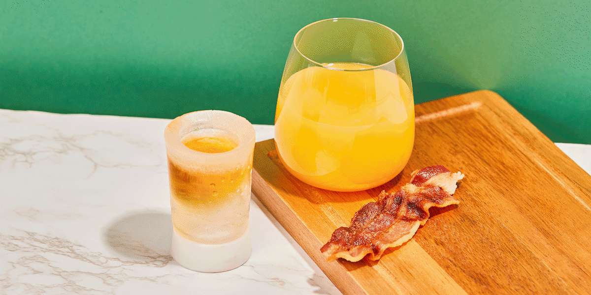A hand grabbing the Irish Breakfast Shot while the orange juice and candied bacon are consumed in stop motion style.