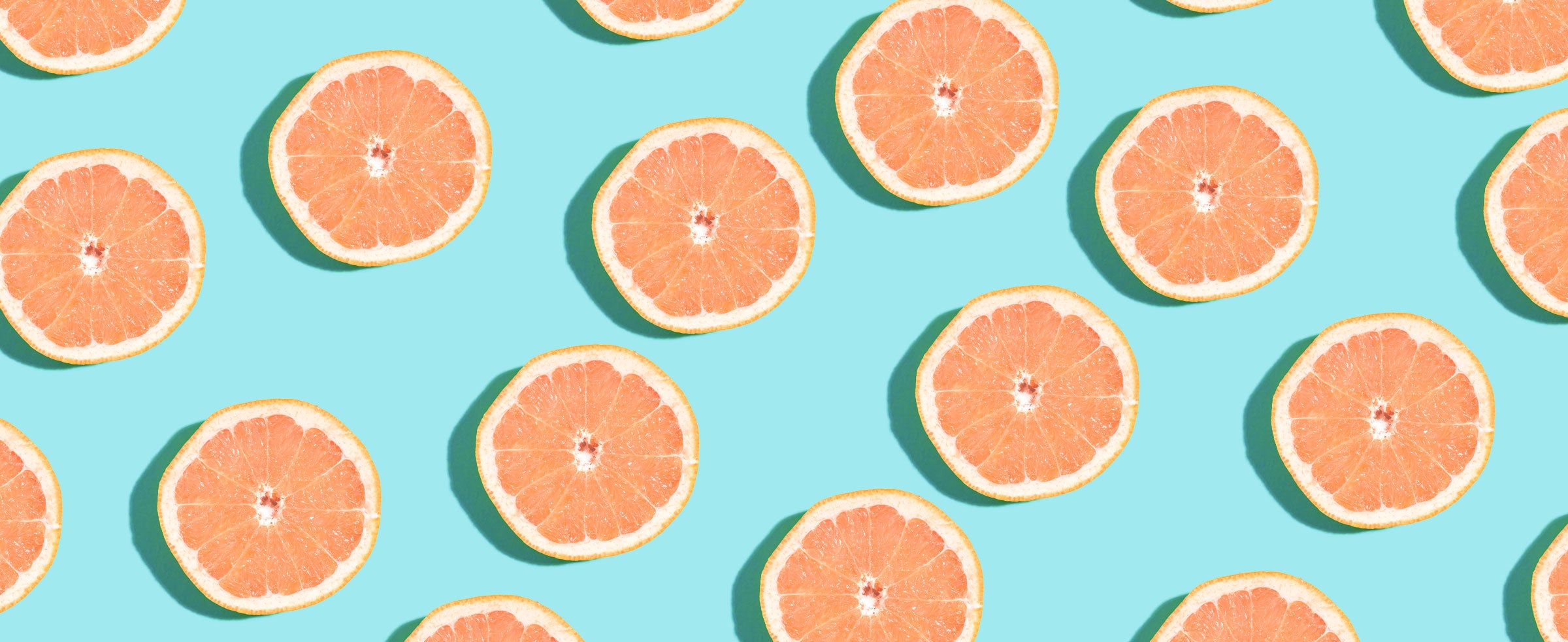 An overhead image of halved grapefruits on a light blue surface.